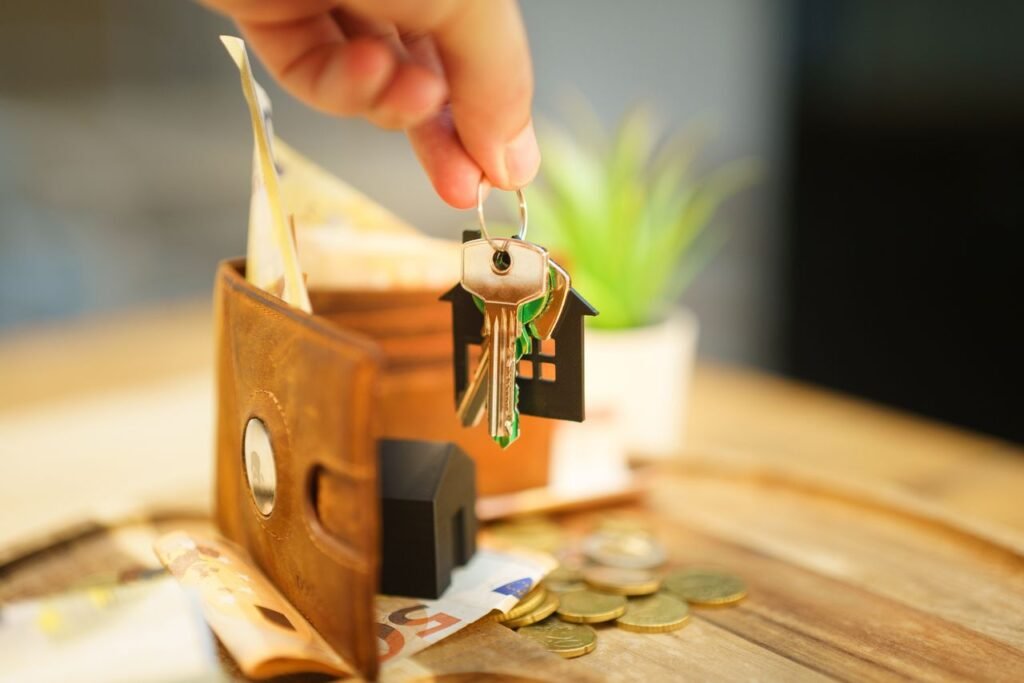 HOME LOAN Close-up of hand holding a house key with a wallet and coins, symbolizing real estate investment.