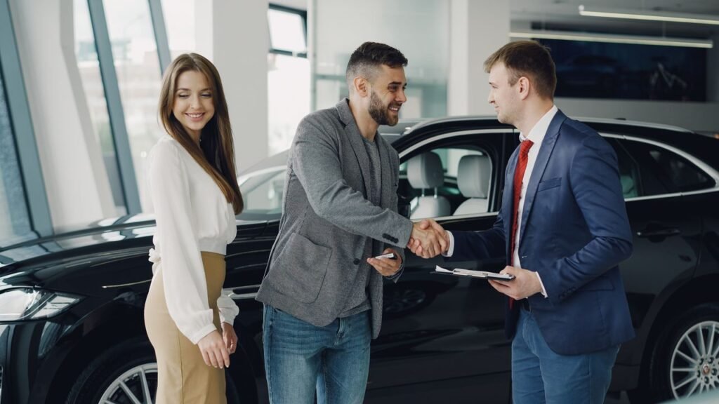 AUTO LOAN USA CARS BAD CREDIT Buyers and sales representative shake hands at a car dealership for a successful car purchase.