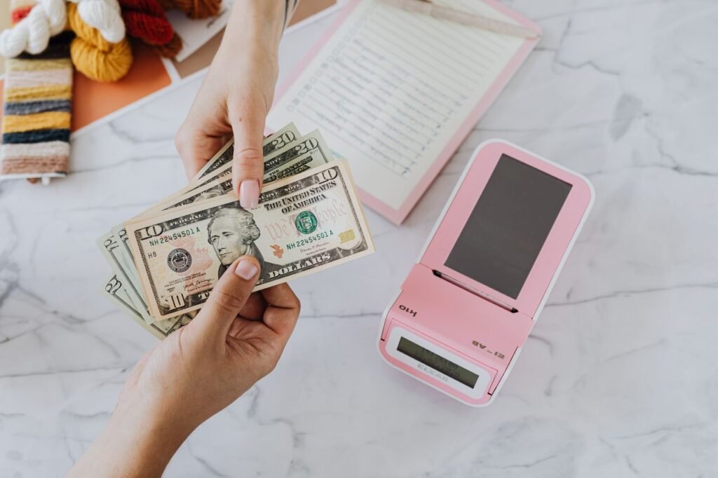 BEST SMALL BUSINESS LOAN Close-up of hands exchanging US dollars with a pink calculator on a marble surface.