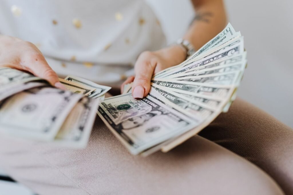 WHAT IS A PERSONAL LOAN Close-up of hands holding and counting US dollar bills indoors.