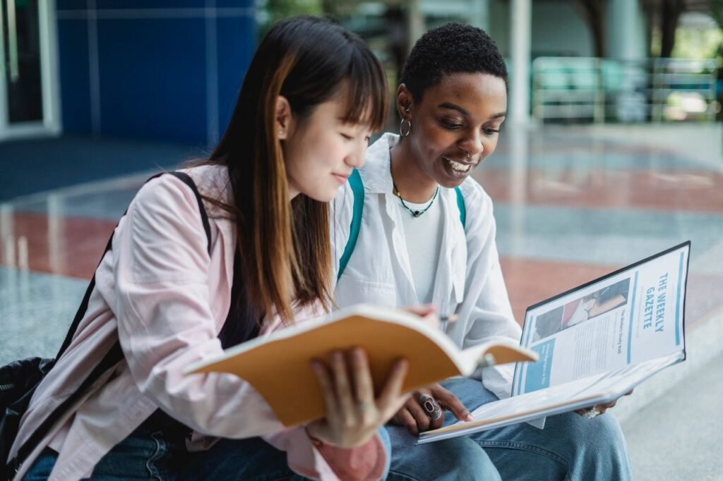STUDENT LOAN INTEREST Young content multiethnic best female friends speaking while watching textbook on street stairs in city