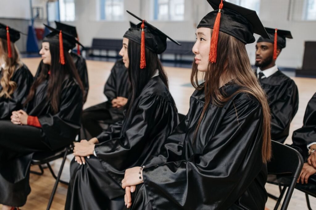 Graduates in caps and gowns seated indoors during a ceremony, celebrating academic success together.