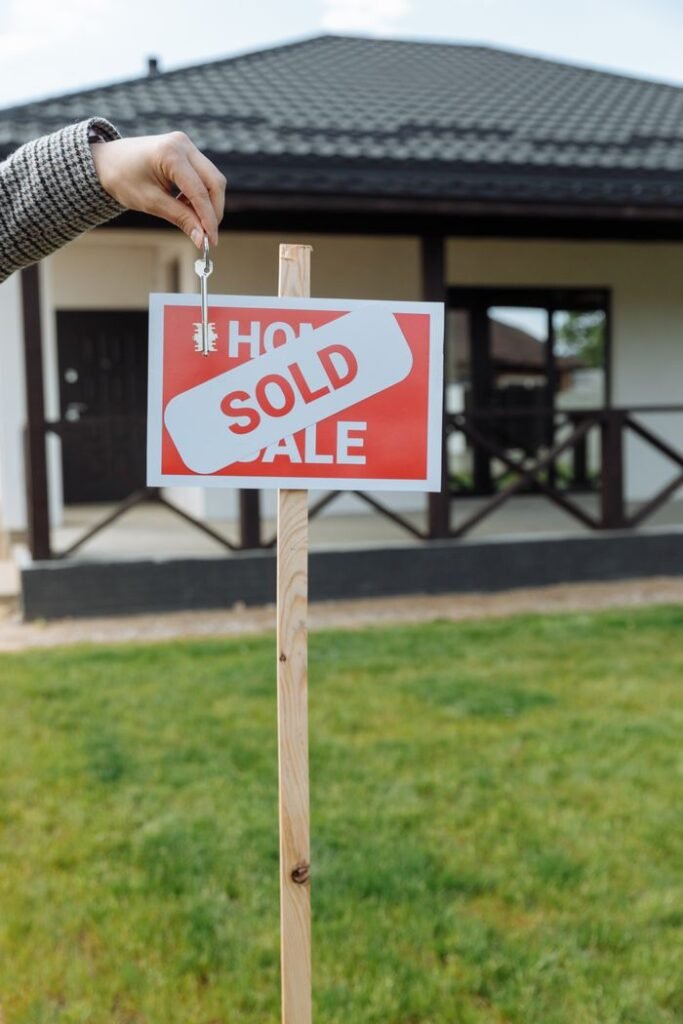 MORTGAGE LOAN RATES A hand holding a key in front of a sold sign and a house, symbolizing a successful real estate transaction.